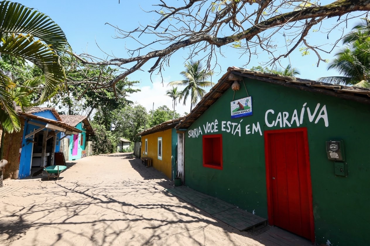 Rua de areia em Caraíva com casinhas coloridas e a frase Sorria você está em Caraíva